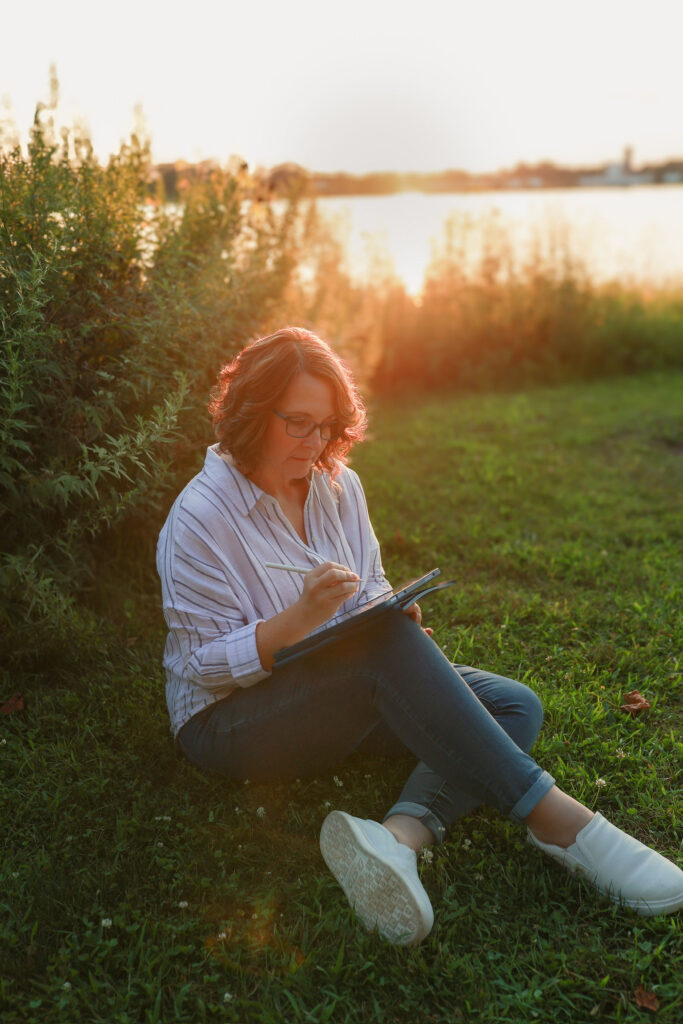 Jamie Eggers writing outdoors by the lake at sunset